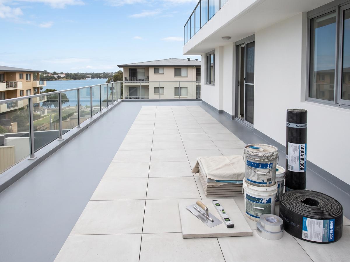 Apartment balcony partway through waterproofing, with membrane rolls, tiles and tools on the deck